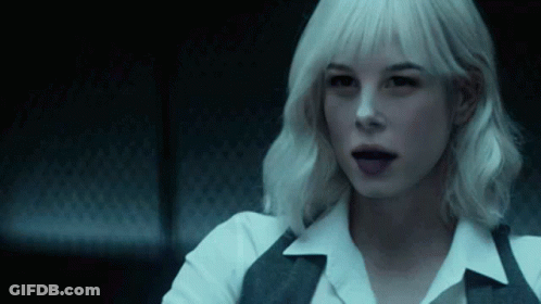 A Woman With White Hair Is Sitting In A Dark Room With Her Tongue Hanging Out . GIF