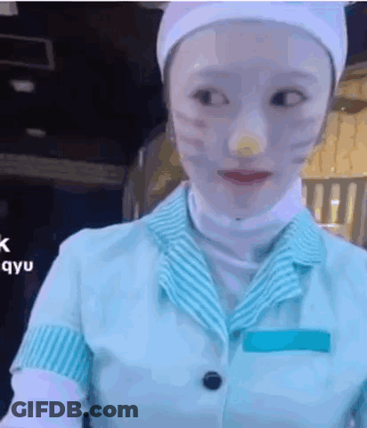 A Woman With White Paint On Her Face Is Wearing A Blue And White Uniform And A White Hat . GIF