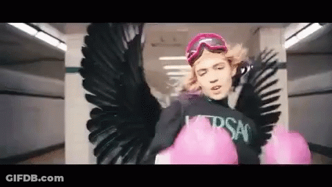 A Woman With Wings And Pink Boxing Gloves Is Wearing A Black Shirt And Goggles . GIF