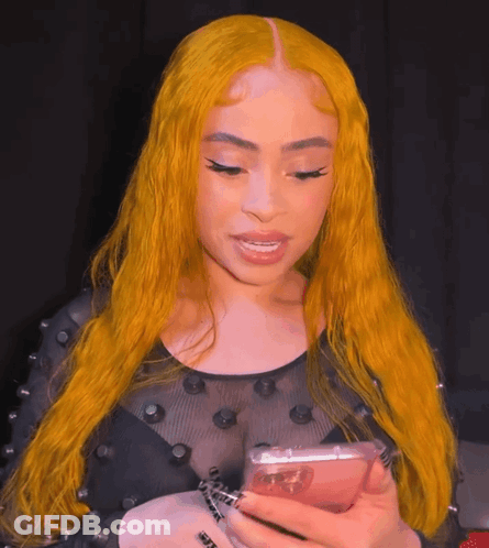 A Woman With Yellow Hair Is Holding A Cell Phone In Her Hand GIF