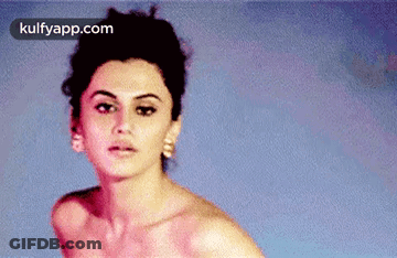 A Woman Without A Shirt Is Standing In Front Of A Blue Wall . GIF