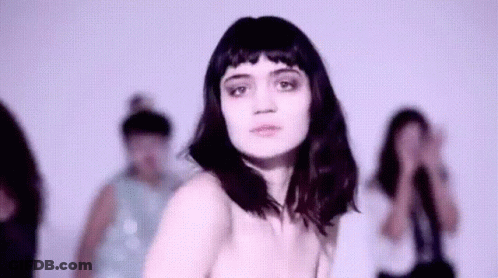 A Woman Without A Shirt Is Standing In Front Of A Group Of People . GIF