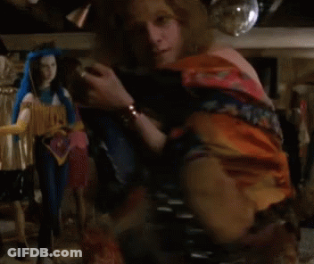 A Woman Without A Shirt Is Standing In Front Of A Shelf With Dolls On It . GIF