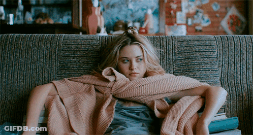 A Woman Wrapped In A Pink Blanket Sits On A Couch With Books GIF