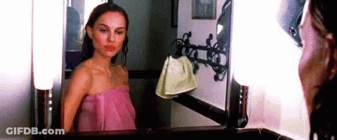 A Woman Wrapped In A Pink Towel Is Standing In Front Of A Mirror . GIF