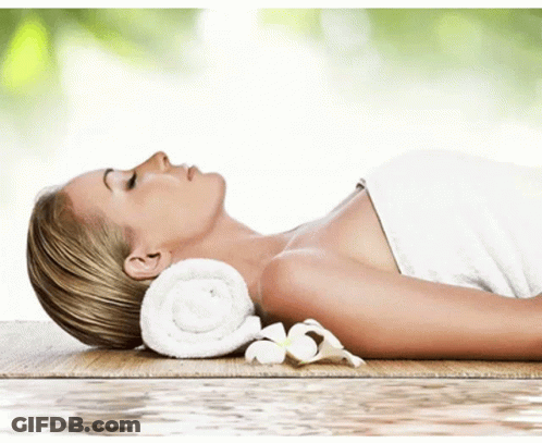 A Woman Wrapped In A Towel Is Laying On A Wooden Table GIF