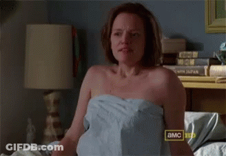 A Woman Wrapped In A Towel Is Sitting On A Bed With A Sign That Says A & Mc GIF