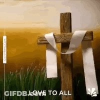 A Wooden Cross With A White Ribbon Around It Is Sitting In The Grass . GIF