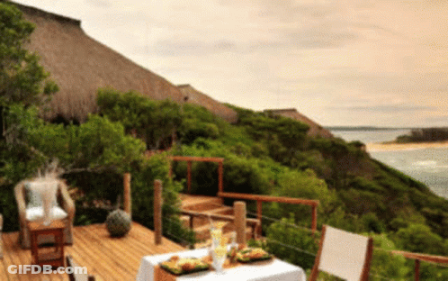 A Wooden Deck With A Table And Chairs Overlooking A Body Of Water GIF