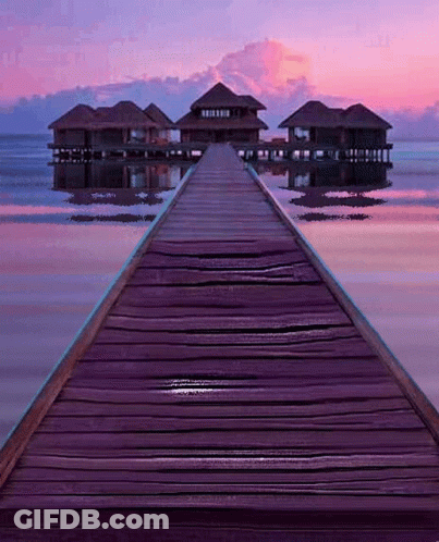 A Wooden Dock Leads To A Small Island With Houses On It GIF