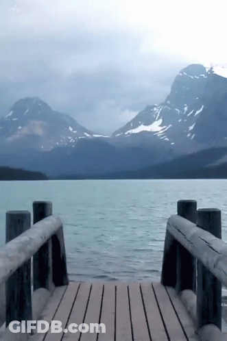 A Wooden Dock With Mountains In The Background And A Lake In The Foreground GIF