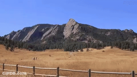 A Wooden Fence Surrounds A Grassy Field With Mountains In The Background GIF