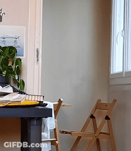 A Wooden Folding Chair Sits Next To A Desk With A Picture On The Wall Above It GIF