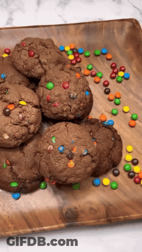A Wooden Plate Topped With Chocolate Cookies And M & Ms GIF