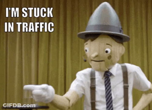 A Wooden Puppet Says I 'M Stuck In Traffic While Pointing A Finger GIF