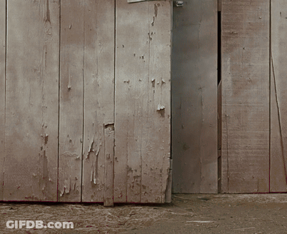 A Wooden Shed With The Door Open And A Few Pieces Of Hay On The Ground GIF