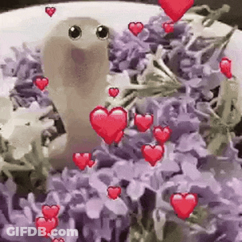 A Worm Is Sitting In A Pile Of Purple Flowers Surrounded By Hearts . GIF