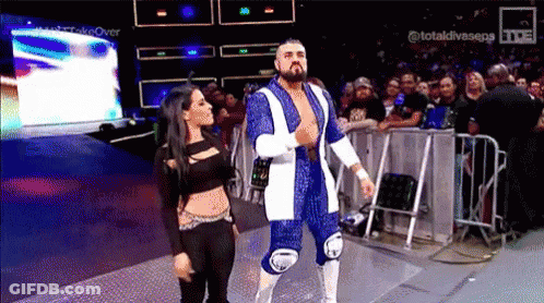 A Wrestler And A Woman Are Walking On A Stage . GIF