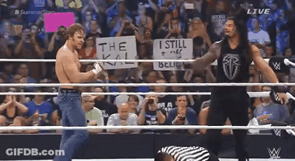 A Wrestler Holding A Sign That Says The Kill Is Standing In A Wrestling Ring With Another Wrestler . GIF