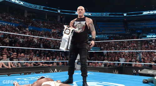 A Wrestler Holds A Trophy In A Wrestling Ring With A Crowd Watching GIF