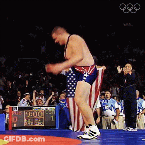 A Wrestler Holds An American Flag In Front Of A Scoreboard That Says " Bud Light " On It GIF