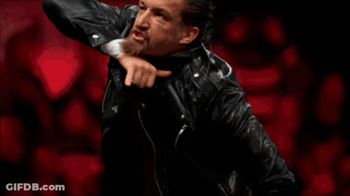 A Wrestler In A Black Leather Jacket Raises His Hand GIF