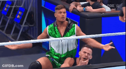 A Wrestler In A Green And White Outfit Is Standing In A Wrestling Ring . GIF