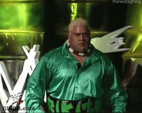A Wrestler In A Green Shirt Stands In Front Of A Sign That Says The Next Big Thing GIF