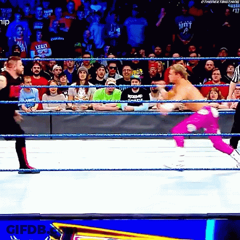A Wrestler In A Pink Outfit Is Jumping Into The Ring While A Crowd Watches GIF