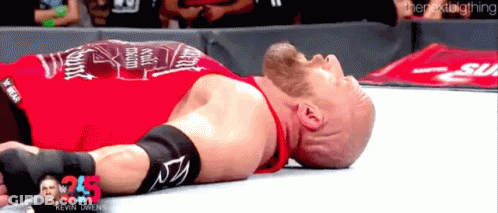 A Wrestler In A Red Shirt Is Laying Down On The Ground GIF
