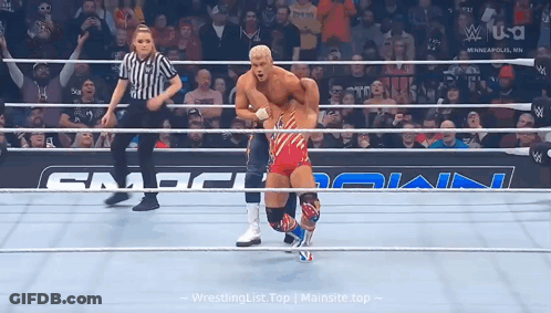A Wrestler In A Red White And Blue Outfit Is In A Ring With A Referee . GIF