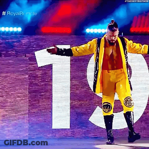 A Wrestler In A Yellow Jacket And Pants Is Standing In Front Of A Sign That Says 19 . GIF