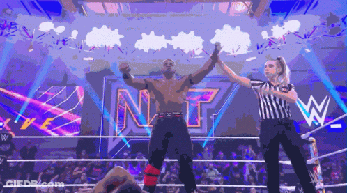 A Wrestler Is Being Congratulated By A Referee In Front Of A Sign That Says Nxt GIF
