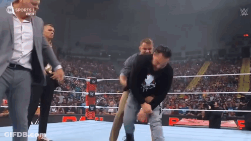 A Wrestler Is Being Helped Out Of The Ring By A Man In A Suit GIF