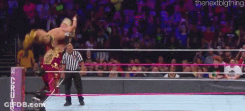 A Wrestler Is Being Lifted In The Air By A Referee In A Wrestling Ring While A Crowd Watches . GIF