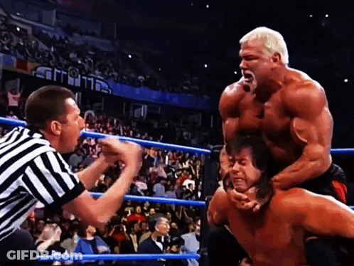 A Wrestler Is Being Lifted Up By Another Wrestler While A Referee Looks On GIF