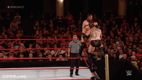 A Wrestler Is Doing A Flip In A Wrestling Ring With The Hashtag #WWE On The Bottom GIF