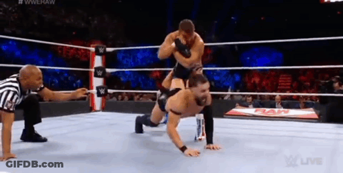 A Wrestler Is Doing Push Ups In A Wrestling Ring While A Referee Looks On . GIF