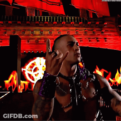 A Wrestler Is Giving The Middle Finger In Front Of A Red Background That Says Thenextbigthing GIF