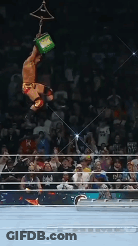 A Wrestler Is Hanging Upside Down In The Air While Holding A Green Box GIF