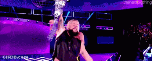 A Wrestler Is Holding A Championship Belt In The Air While Standing On A Stage . GIF