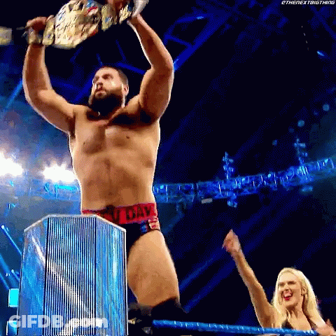A Wrestler Is Holding A Championship Belt Over His Head While A Woman Watches . GIF