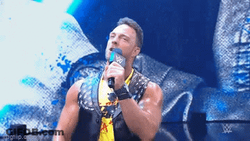 A Wrestler Is Holding A Microphone In His Hand And Talking Into It On A Stage . GIF