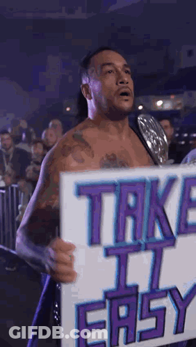 A Wrestler Is Holding A Sign That Says Take It Easy . GIF