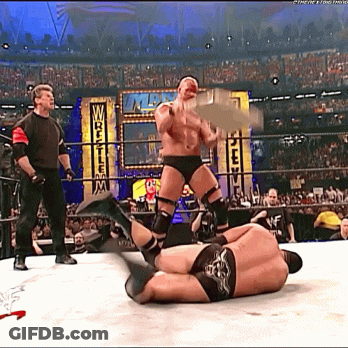 A Wrestler Is Holding A Trophy While Another Wrestler Is Laying On The Floor GIF