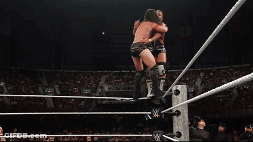 A Wrestler Is Jumping Over A Rope In A Wrestling Ring With A Crowd Watching GIF
