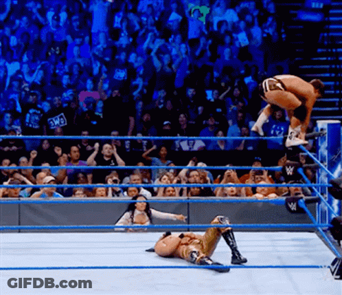 A Wrestler Is Jumping Over Another Wrestler While A Crowd Watches GIF