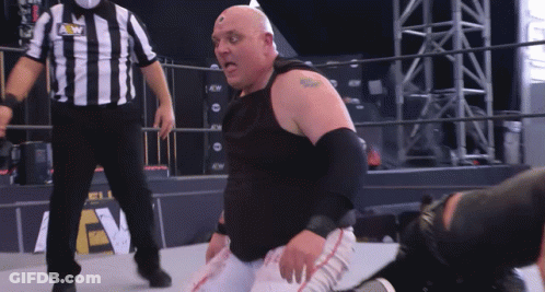 A Wrestler Is Kneeling Down In Front Of A Referee Wearing A Shirt That Says Aew GIF