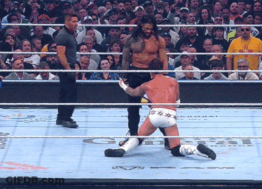 A Wrestler Is Kneeling Down In The Ring While A Referee Looks On GIF