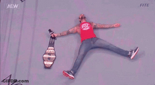 A Wrestler Is Laying On The Floor With A Microphone And A Championship Belt . GIF